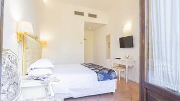 A hotel room with a bed, a bedside table, a chair, a desk, a television, and a window with curtains.