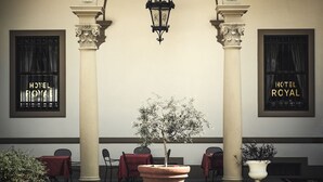 A hotel lobby with columns, a central tree, and tables with red tablecloths. - Villa Royal (Florence)