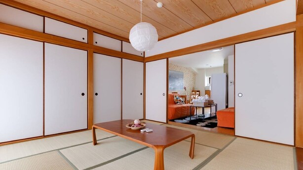 Une pièce de style japonais traditionnel, avec un sol recouvert de tatamis, une basse table en bois, des portes coulissantes et un luminaire suspendu.