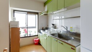 Une cuisine avec des meubles de couleur verte, un évier en acier inoxydable et une fenêtre donnant sur un jardin fleuri.