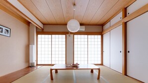 Une pièce de style japonais traditionnel, avec un sol recouvert de tatamis, une basse table en bois, des portes coulissantes et un ventilateur de plafond.