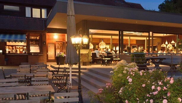 Un espace extérieur aménagé avec des tables et des bancs, un bar et un bâtiment doté de grandes fenêtres.