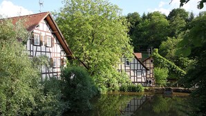 Une maison traditionnelle à colombages, située au bord d’une rivière paisible et entourée d’une végétation luxuriante.