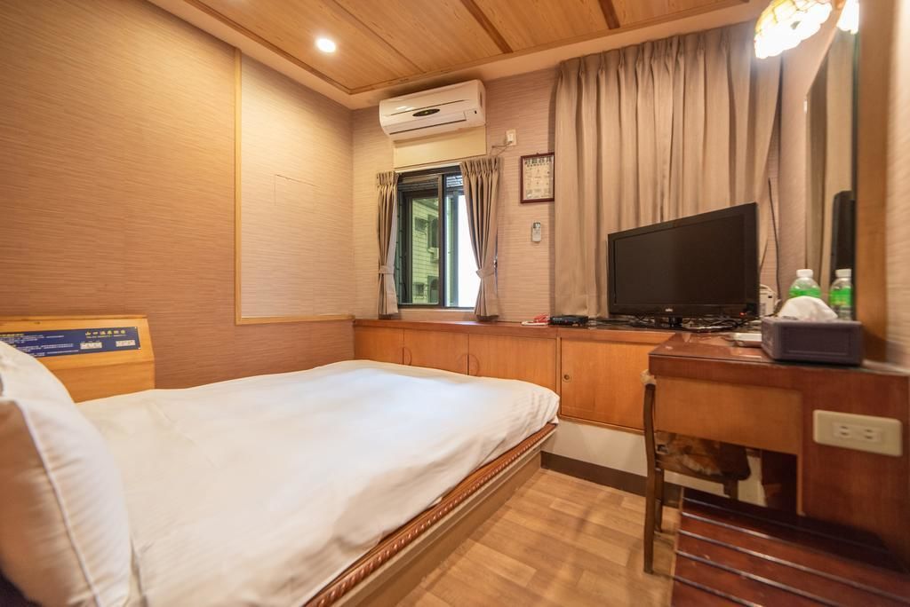 Una habitación de hotel con cama, escritorio con ordenador, aire acondicionado y ventana con cortinas.