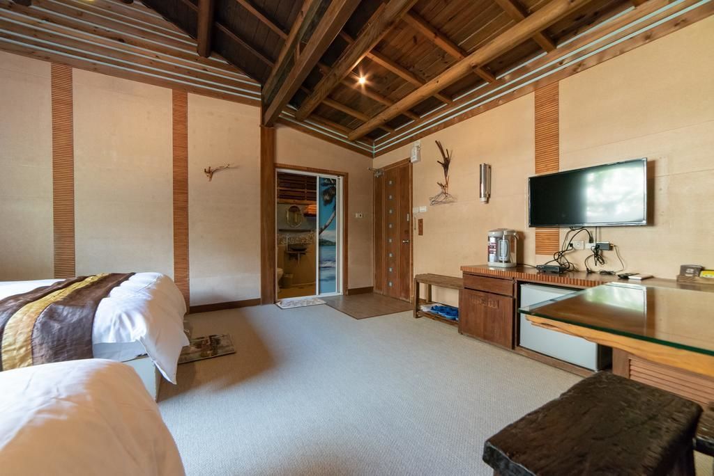 A hotel room with a bed, a desk with a glass top, a television, and a wooden ceiling.
