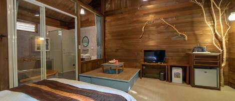 A wooden cabin room with a bed, a TV, a small table, and a mirror.