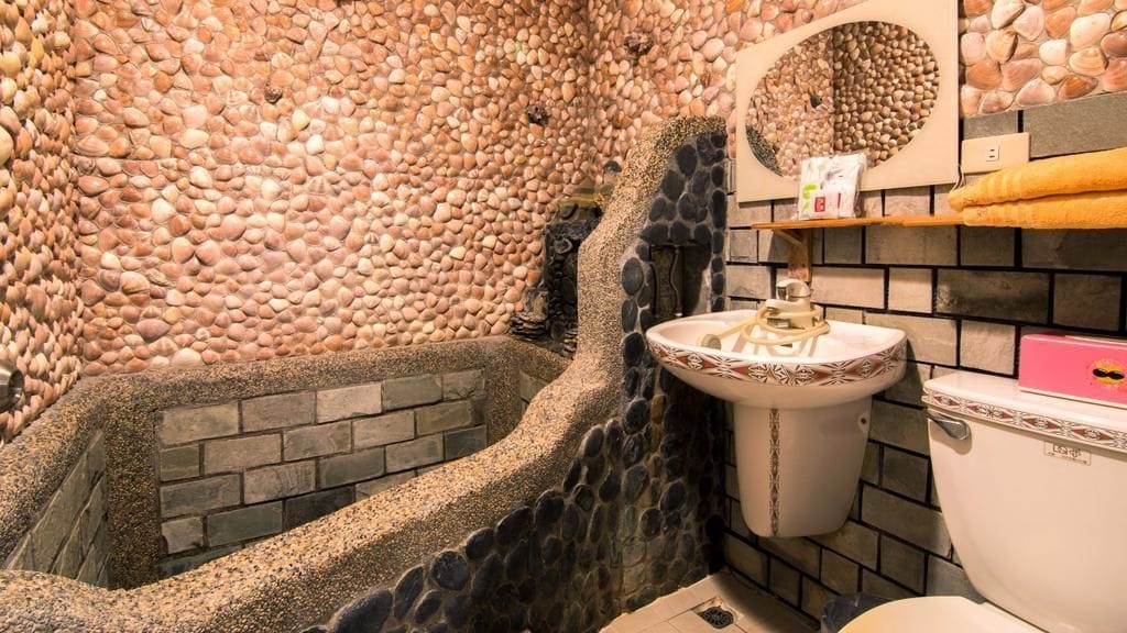 Une salle de bain avec un mur en pierre, une baignoire, un lavabo et des toilettes.