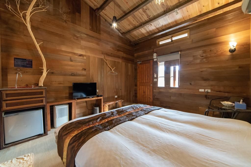 A wooden cabin room with a bed, a television, a small refrigerator, and a wooden tree decoration.