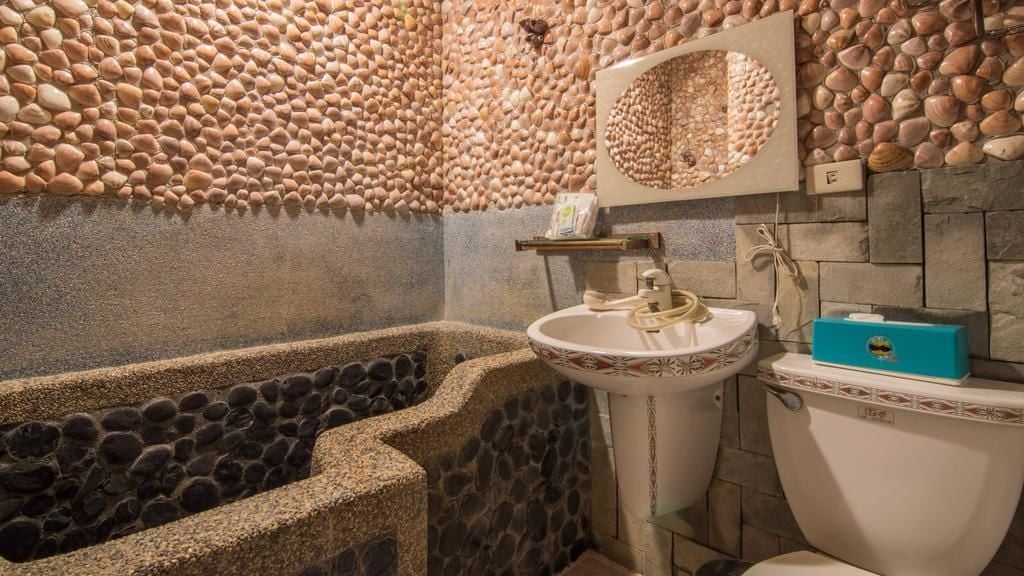 Une salle de bain avec un mur recouvert de petits galets, une baignoire, un lavabo et des toilettes.