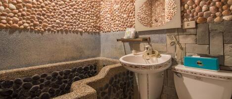 Un baño con pared de piedras, una bañera, un lavamanos y un inodoro.