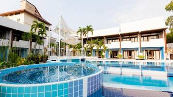 A hotel with a large swimming pool, palm trees, and a modern building with multiple balconies.