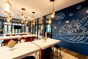 A modern restaurant interior with marble tables, hanging pendant lights, and a wall mural depicting a bowl of food. - Kochira (Hua Hin)