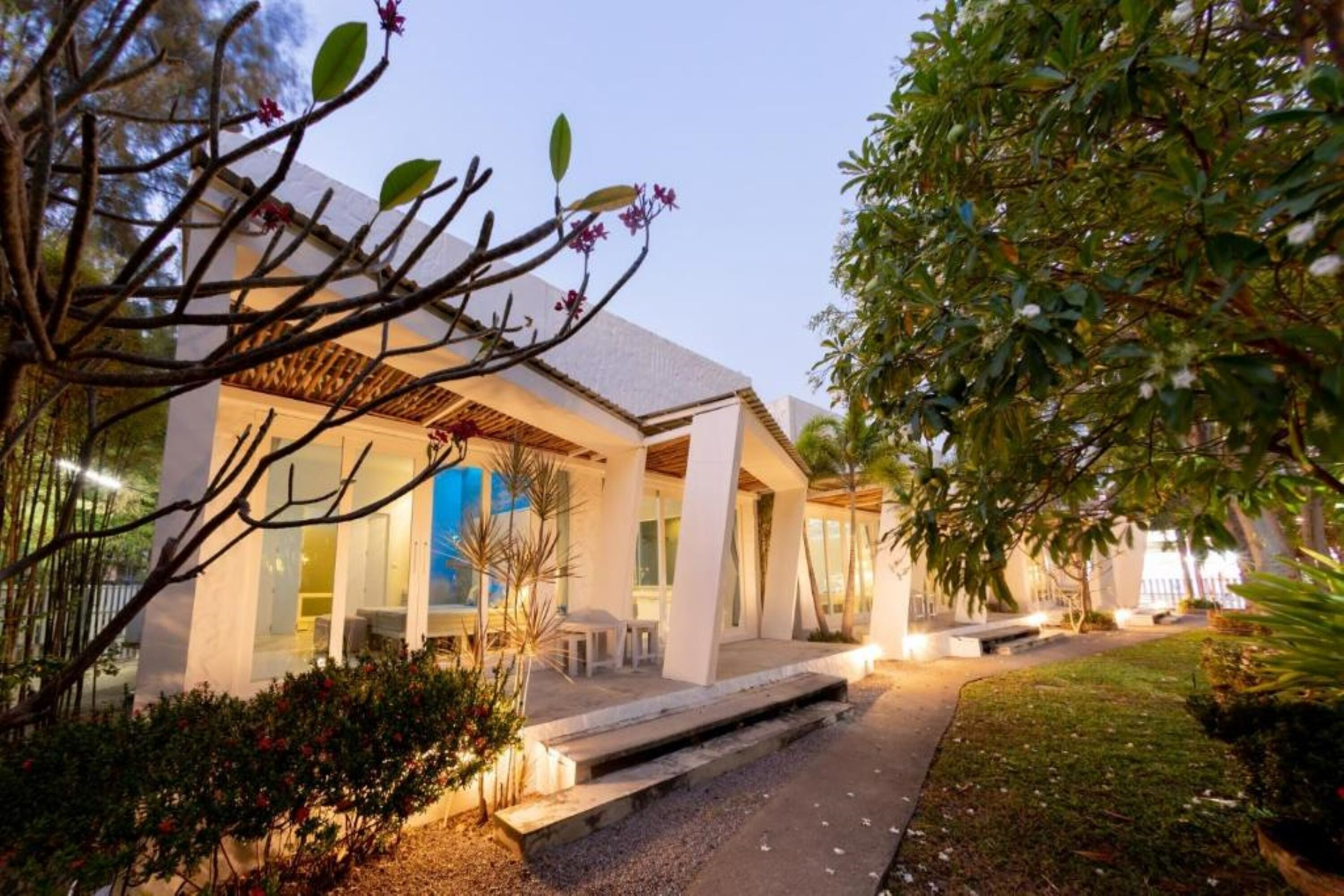 A modern house with a covered patio, a well-maintained garden, and a clear view of the interior through large windows.