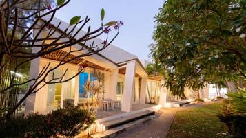 A modern house with a covered patio, a well-maintained garden, and a clear view of the interior through large windows.