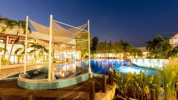 A swimming pool area with a wooden deck, a covered seating area, and a view of the surrounding landscape.