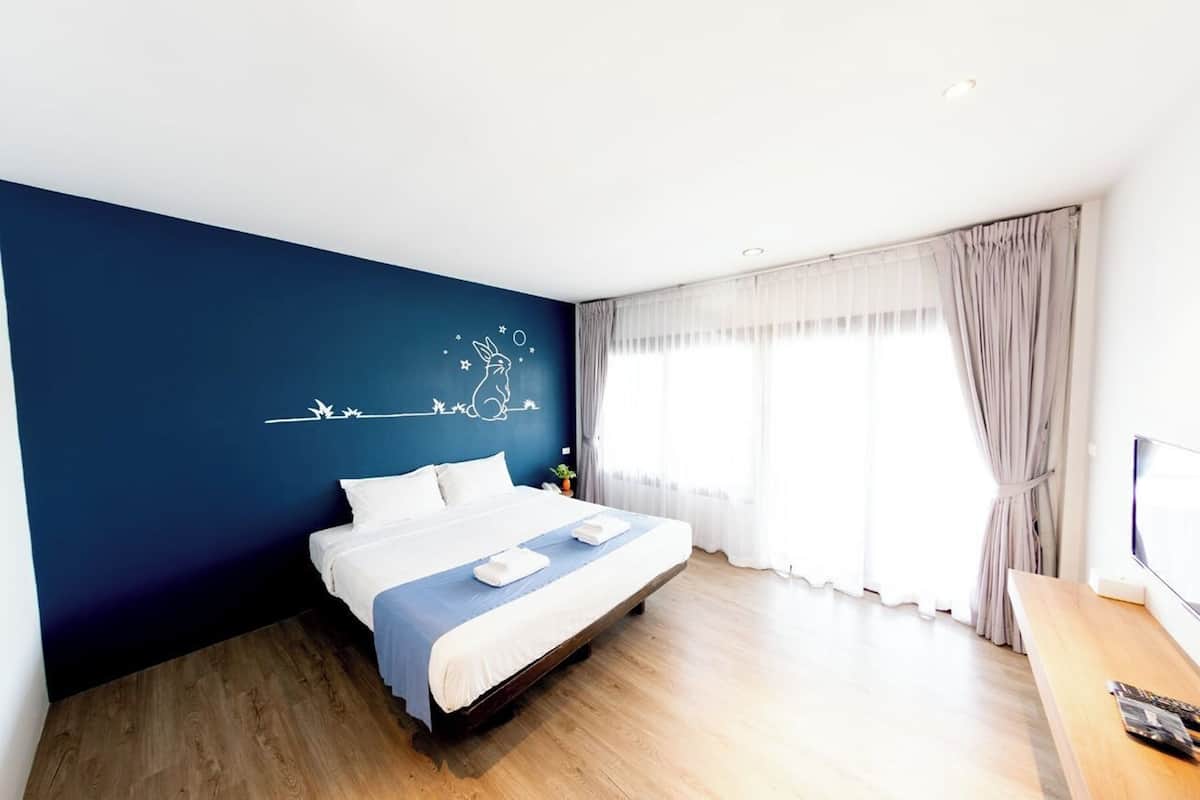 Habitación de hotel moderna con una cama grande, piso de madera, pared de acento azul y una ventana con cortinas.