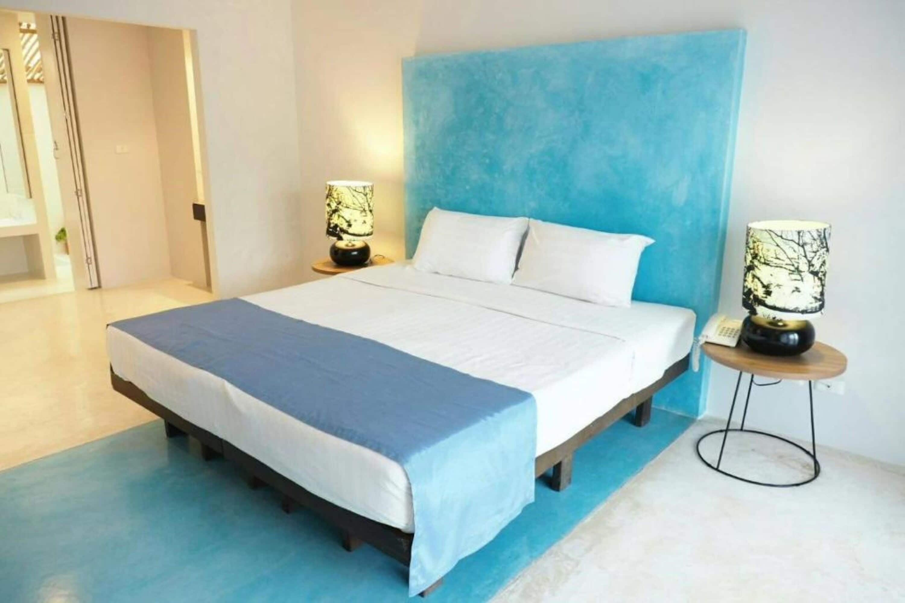 A neatly made bed with a blue bedspread and white pillows, two bedside lamps, and a small round table with a phone.