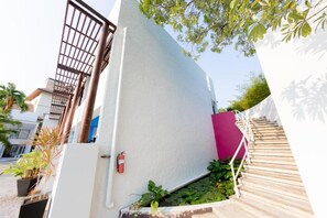 A white building with a metal gate, a fire extinguisher, and a staircase with a pink wall. - Kochira (Hua Hin)