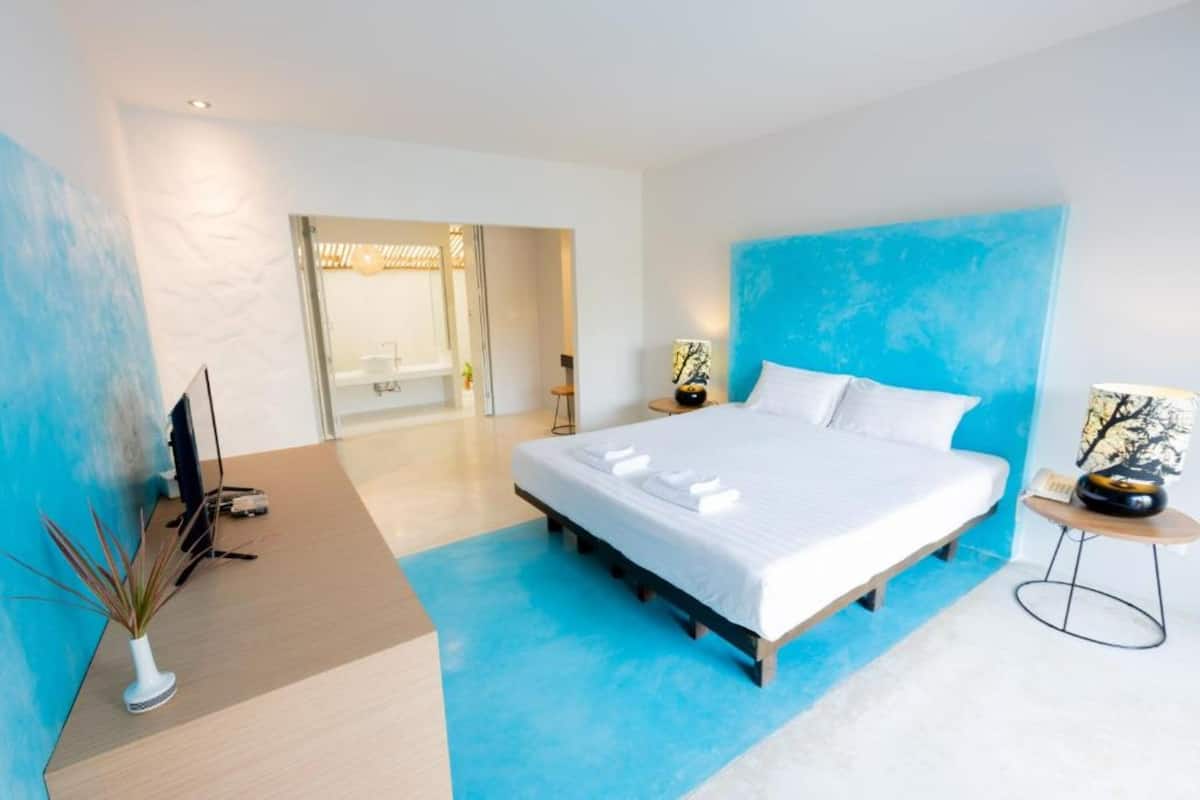 Habitación de hotel moderna con una cama grande, un escritorio y un baño visible a través de una puerta abierta.