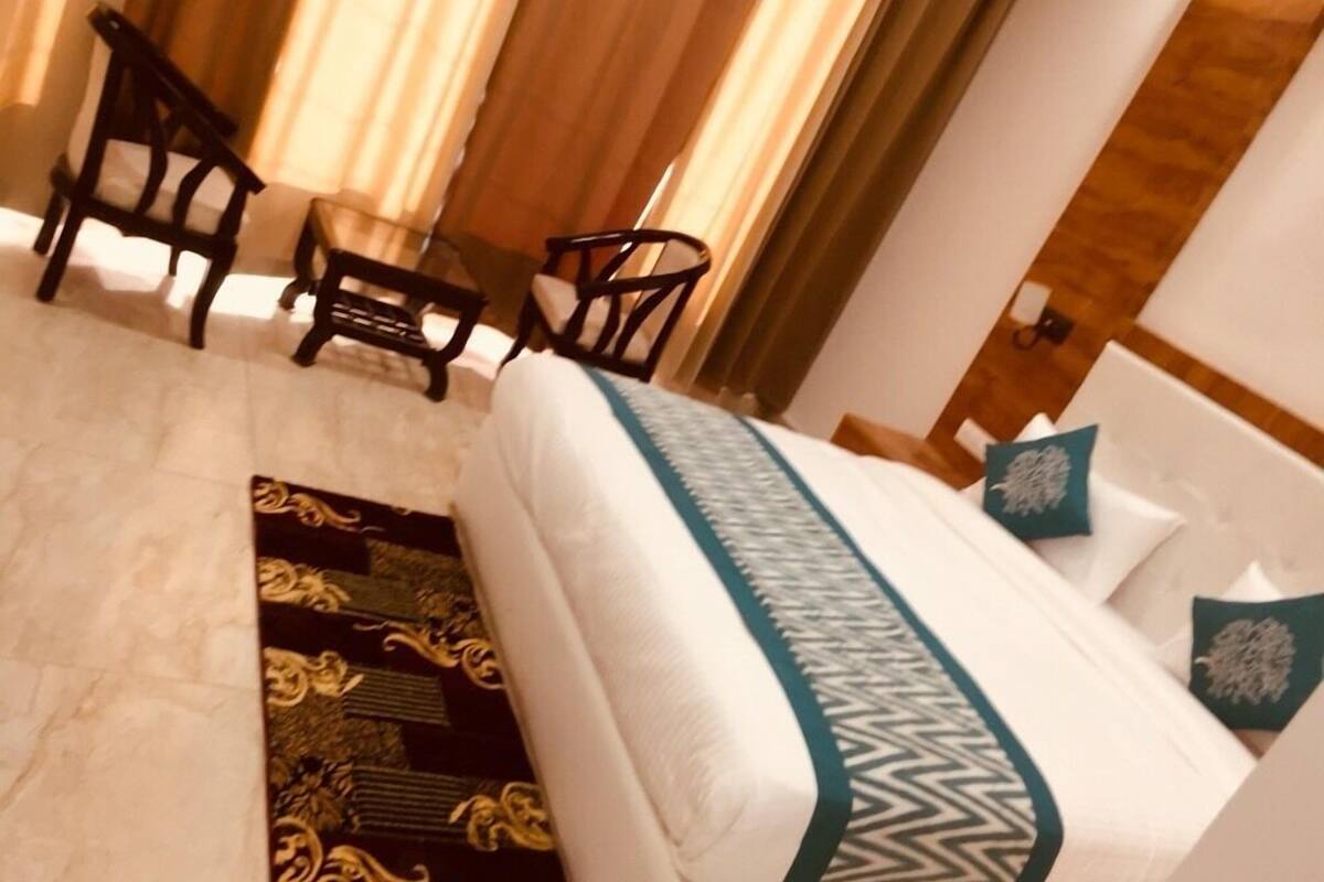 A hotel room with a bed, two chairs, a small table, and a window with curtains.
