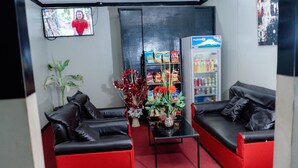 Una hall con due divani in pelle nera, un tavolino, una televisione, una macchina per snack e una pianta in vaso.