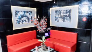Una hall moderna con divani rossi, un tavolino da caffè nero con oggetti decorativi e opere d'arte astratta alle pareti.