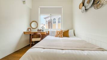 A bedroom with a bed, a desk, a chair, a window, and a view of buildings outside.