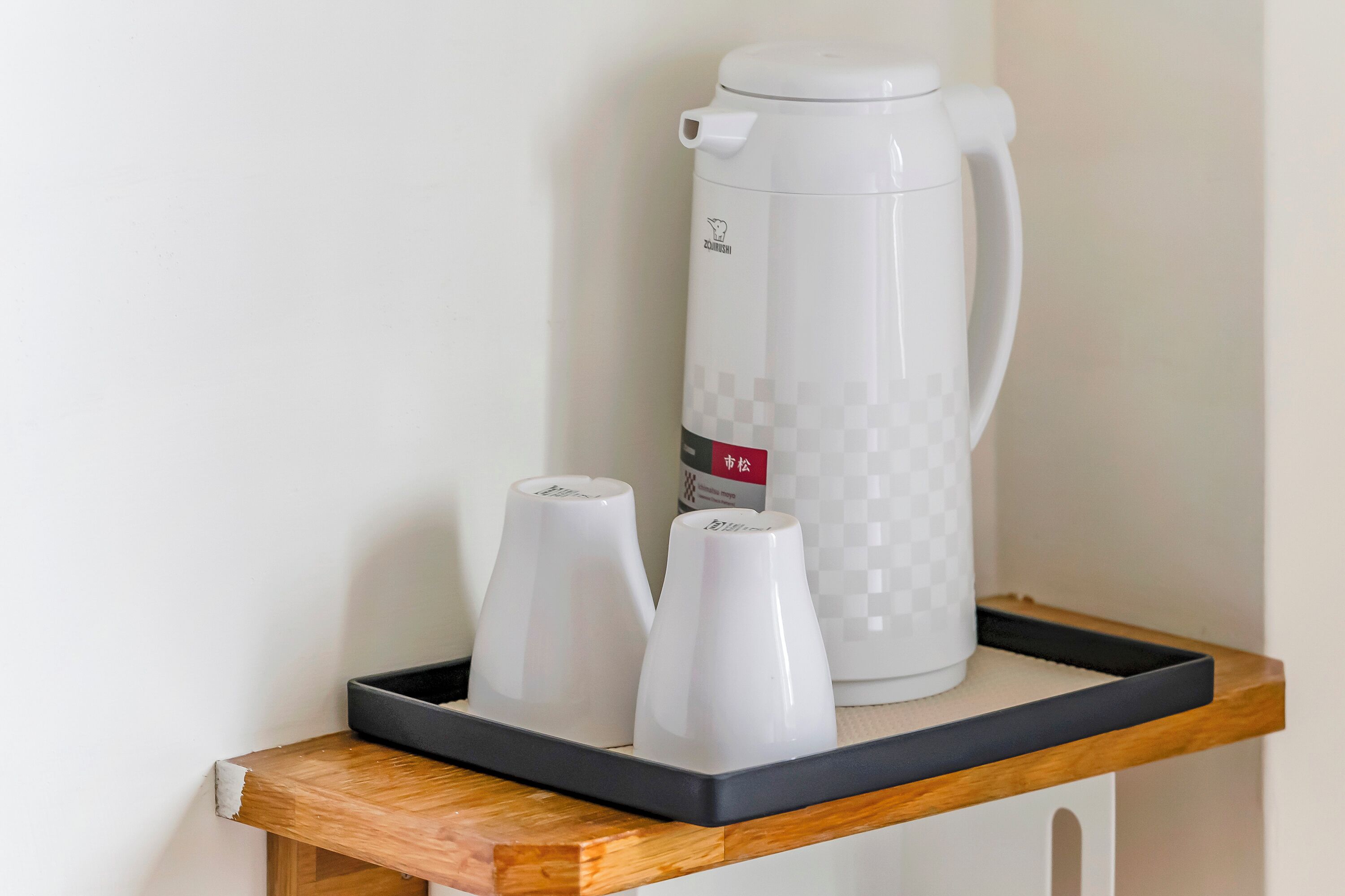 Une machine à café et deux tasses sur un plateau, posés sur une étagère en bois.