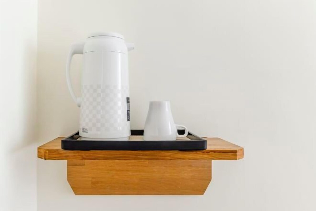A white coffee maker, a white mug, and a white cup on a wooden tray on a wall-mounted shelf.
