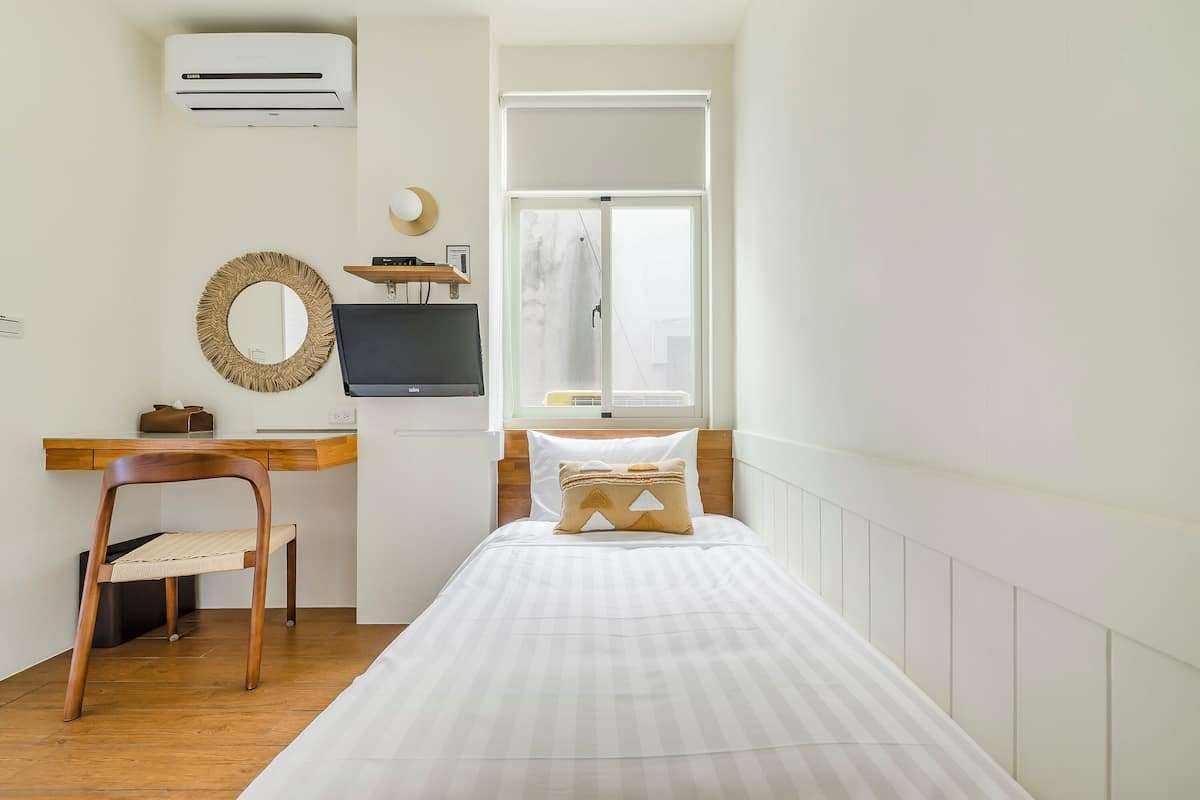 A bedroom with a bed, a desk with a computer, a chair, a television, and a window with a view.