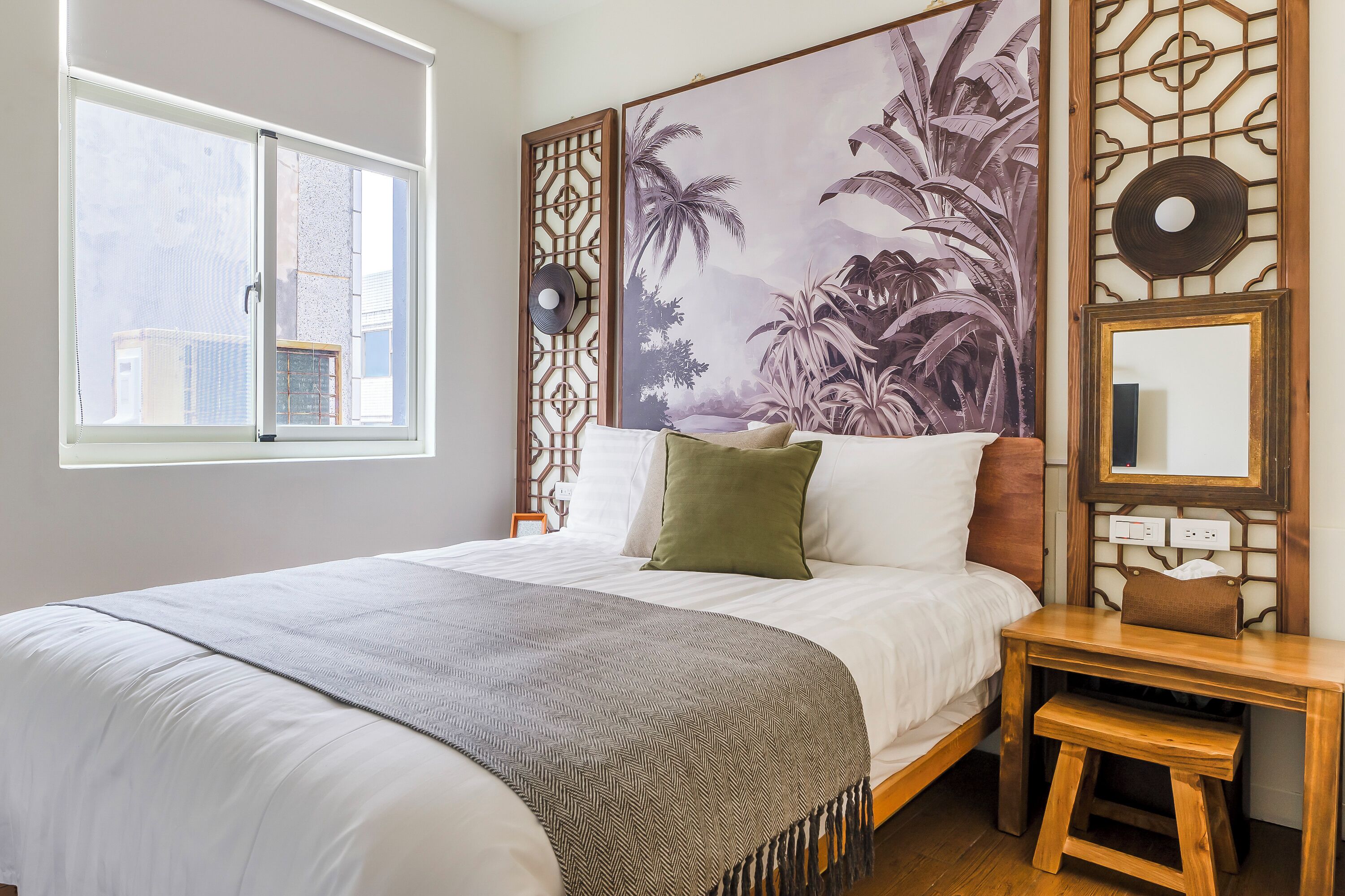 A neatly made bed with a patterned throw, a small wooden table, and a wall-mounted mirror.