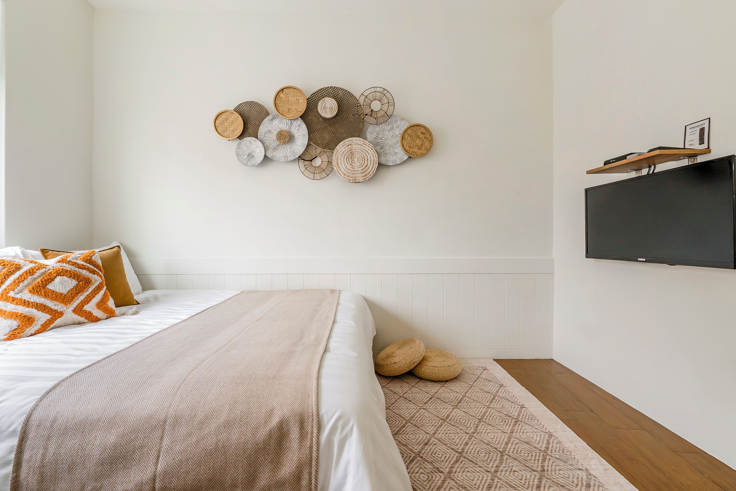 Un dormitorio con cama, almohadas, una colcha, un televisor montado en la pared y un adorno decorativo en la pared.