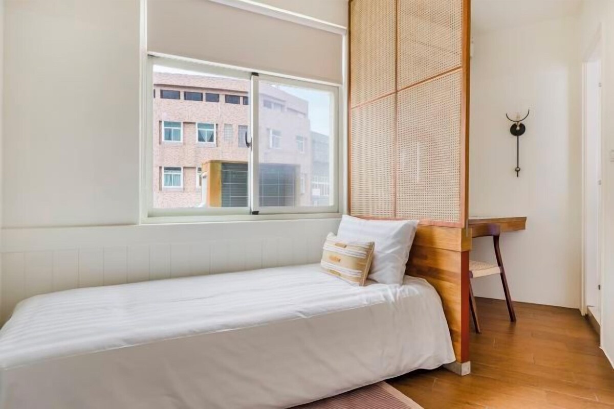 A minimalist bedroom with a single bed, a large window, and a woven partition.