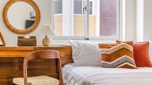 A hotel room with a wooden desk, a chair, a bed with white and patterned pillows, and a window with a view of a brick building. - Chin Style Easy Stay (Magong)