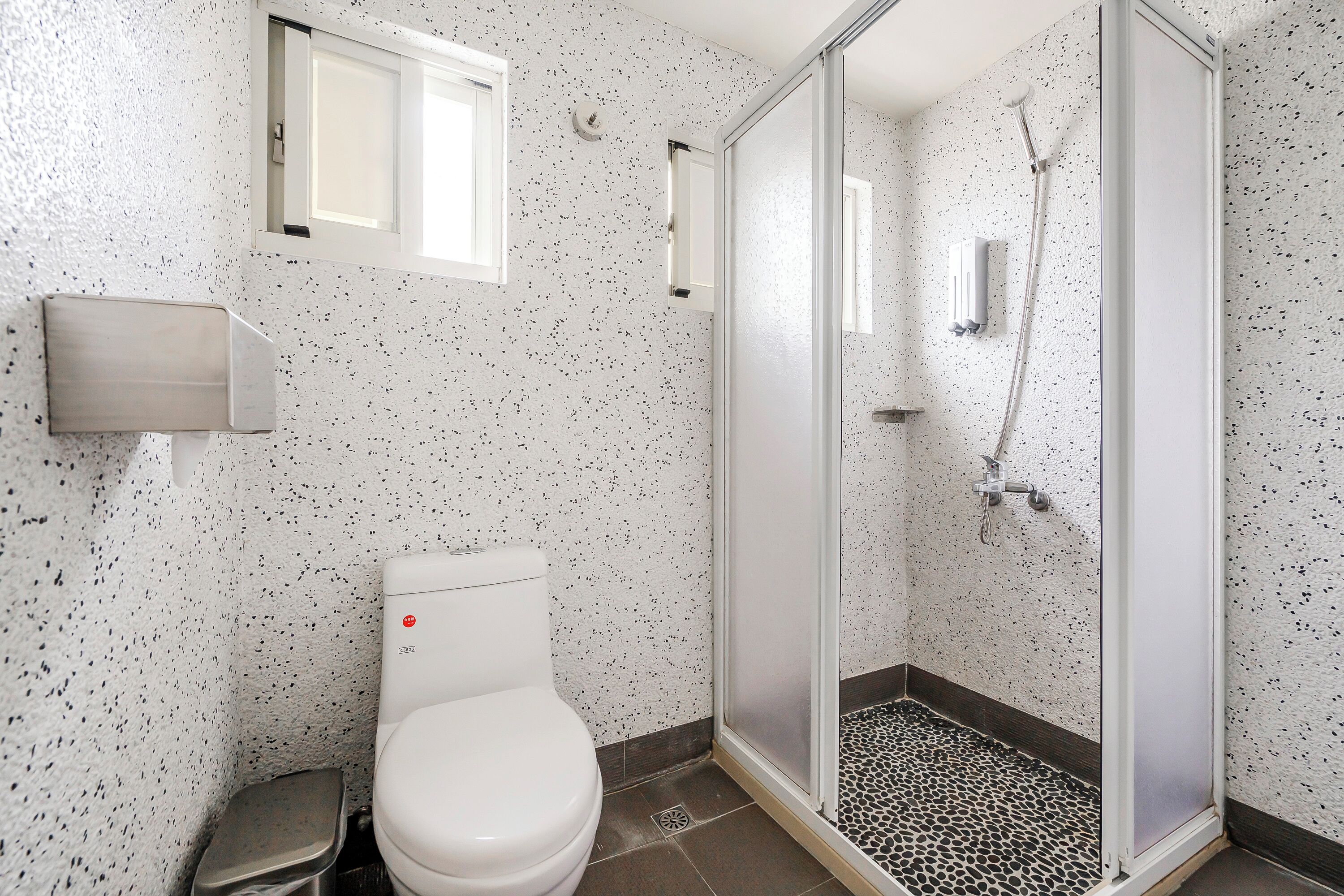 A modern bathroom with a toilet, a shower with a glass door, and a small window above the toilet.