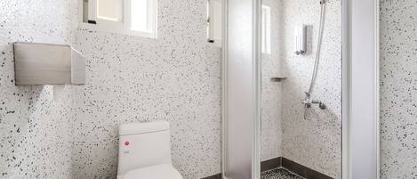 A modern bathroom with a toilet, a shower with a glass door, and a small window above the toilet.