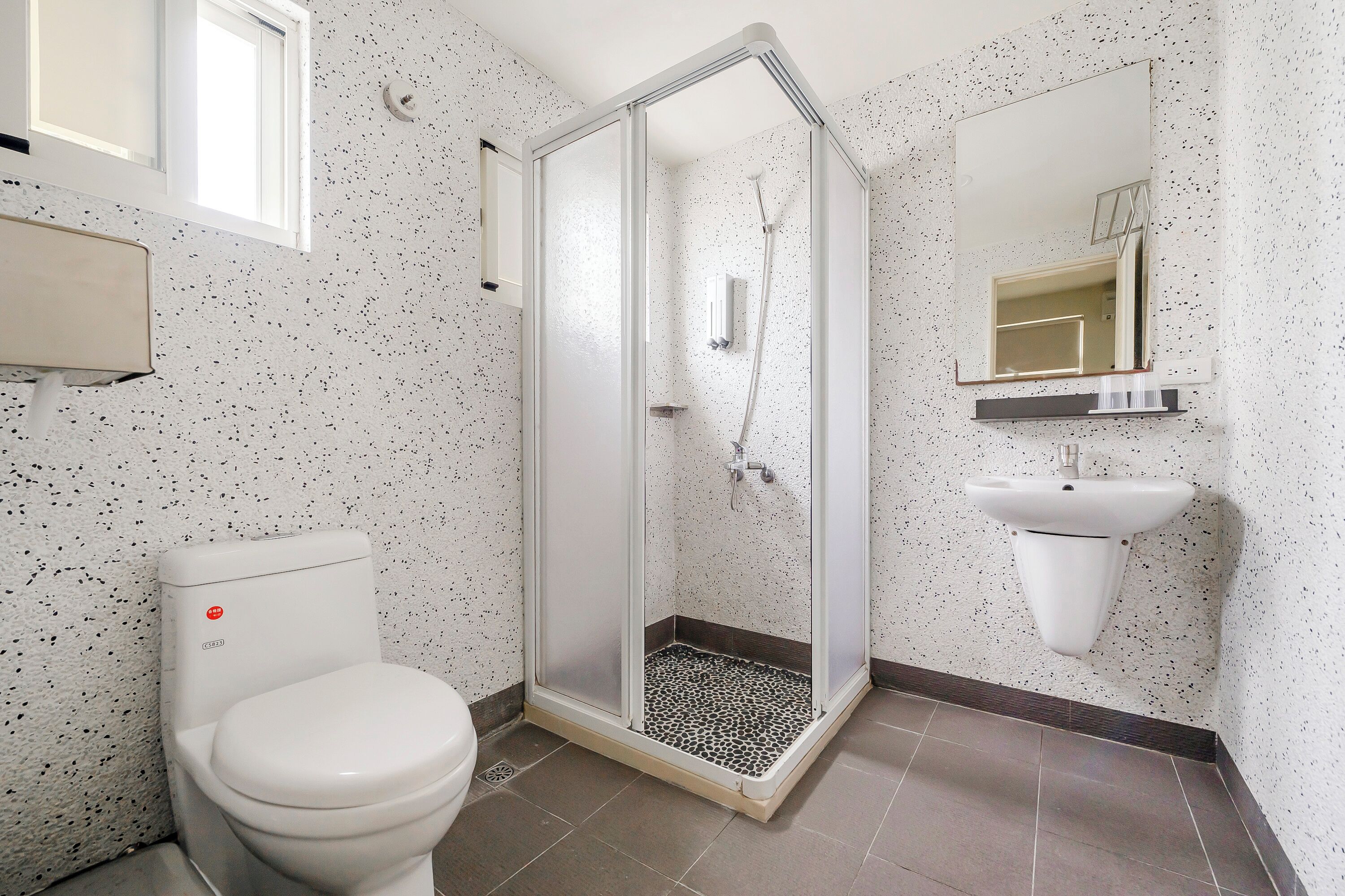 A bathroom with a toilet, a shower with a glass door, a sink, and a mirror.