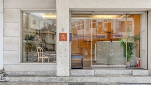A hotel entrance with a glass door, a small outdoor seating area with chairs and a table, and a fire extinguisher visible inside. - Chin Style Easy Stay (Magong)