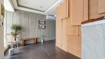 A room with a wooden bench, a potted plant, a wall-mounted clock, and a large window.