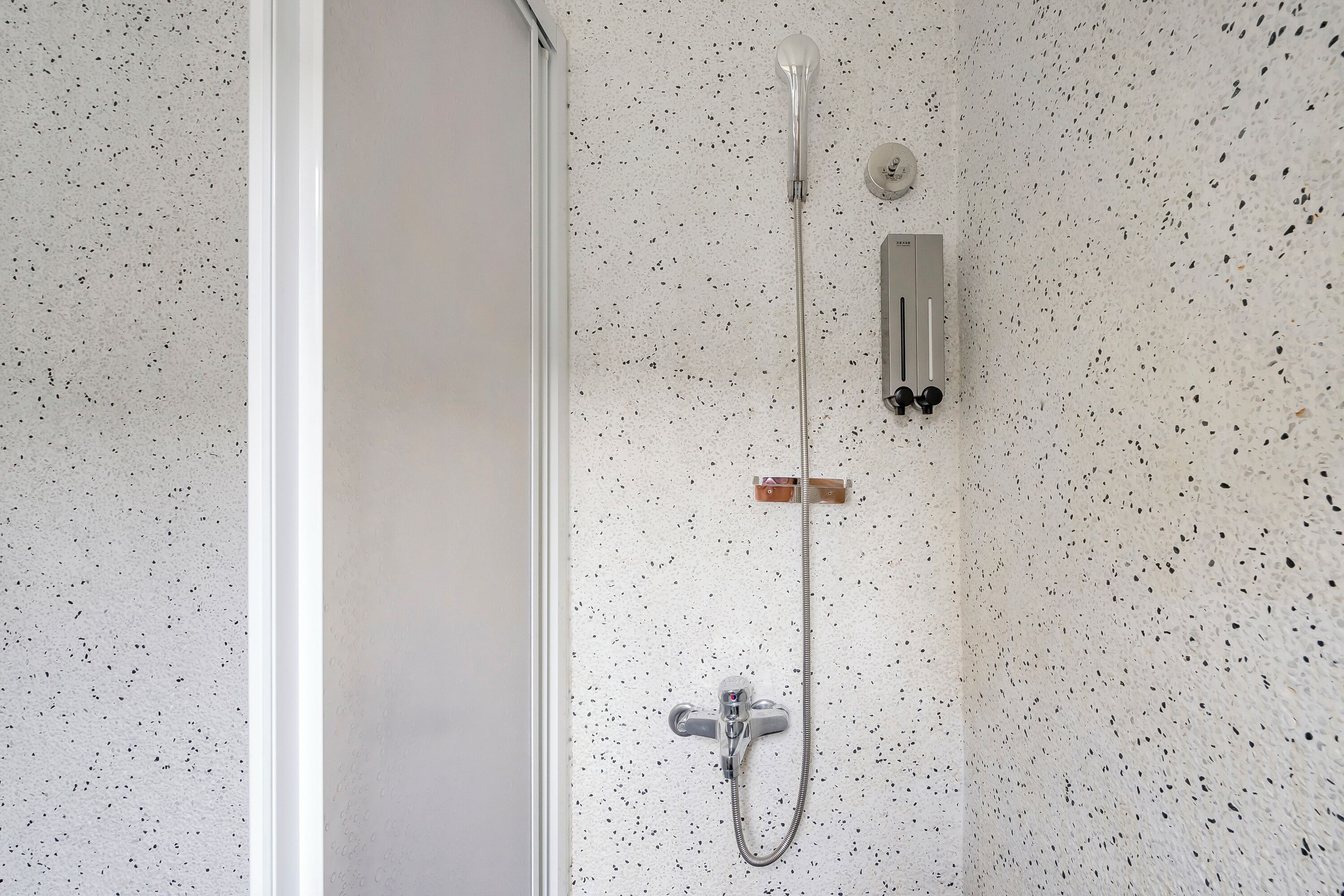 A shower with a handheld showerhead and a wall-mounted control panel.