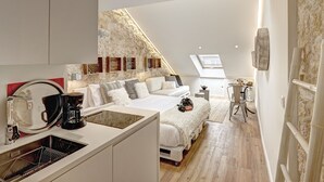 A modern loft bedroom with a skylight, a kitchenette, and a stone wall. - Sonel Investe Apartments Madalena 287 Studios (Lisbon)