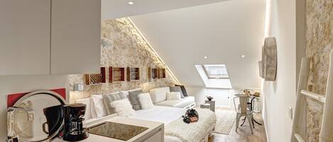 A modern loft bedroom with a skylight, a kitchenette, and a stone wall.