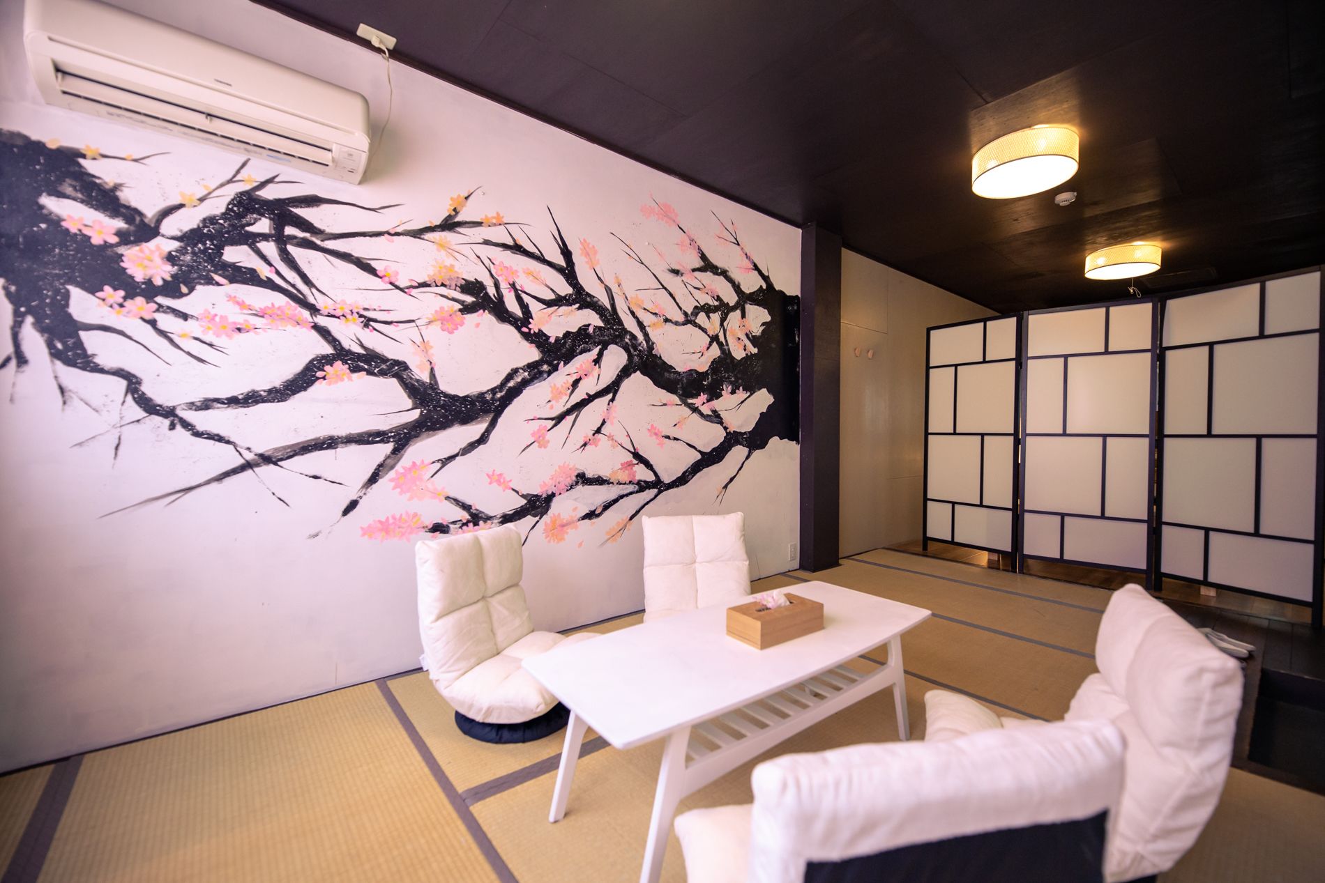 A room with a large wall mural of cherry blossoms, a white sofa, a small table, and a traditional Japanese sliding door.