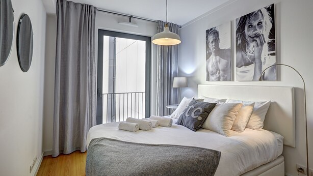 Ein modernes Schlafzimmer mit einem großen Bett, grauen Vorhängen und Blick auf die Stadt.