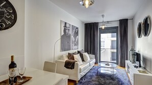 Ein modernes Wohnzimmer mit einem weißen Sofa, einem Esstisch mit Flasche und Gläsern, einem blauen Teppich und einer großen Wanduhr.