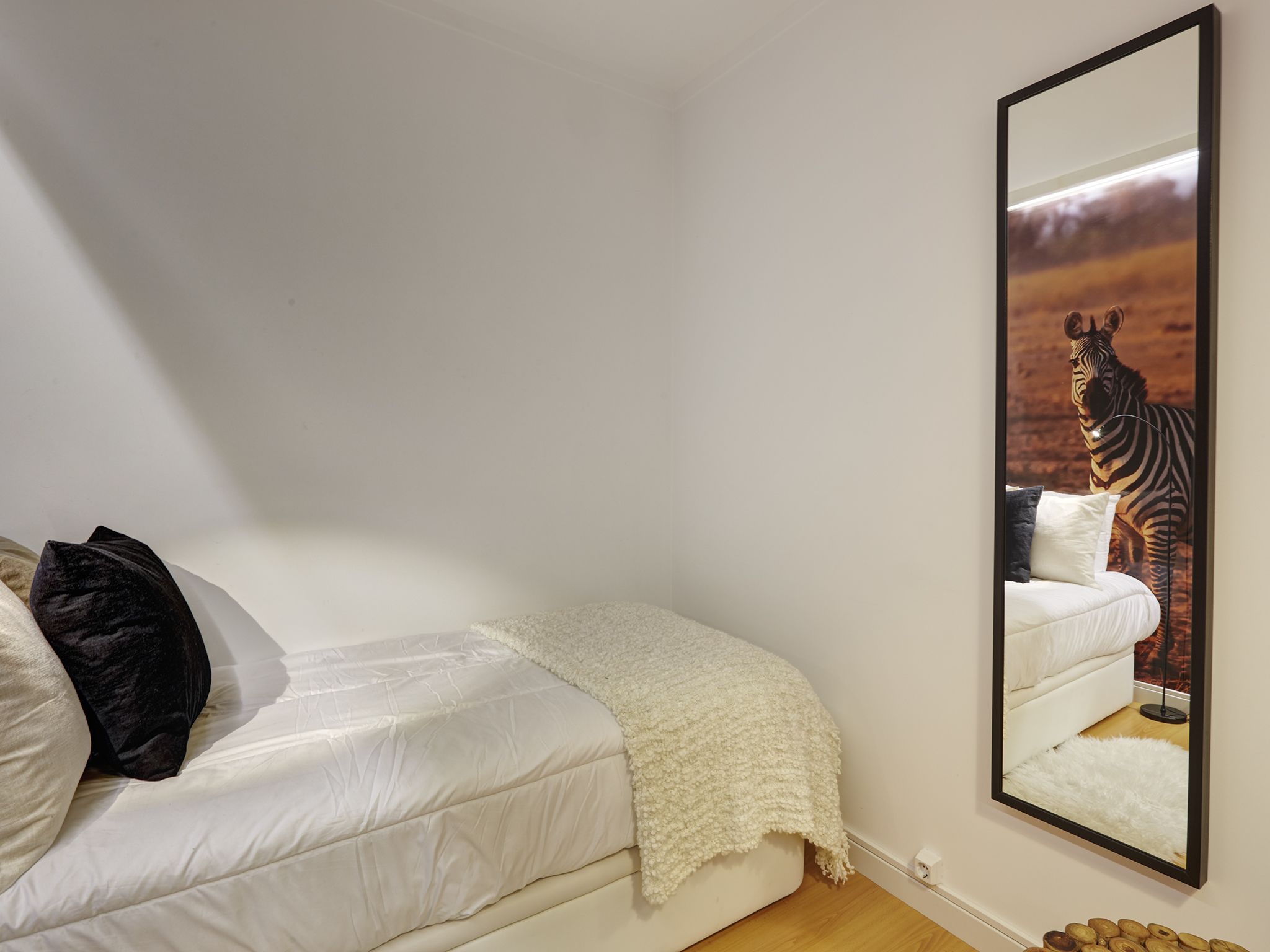A bedroom with a bed, a large mirror, and a zebra painting on the wall.