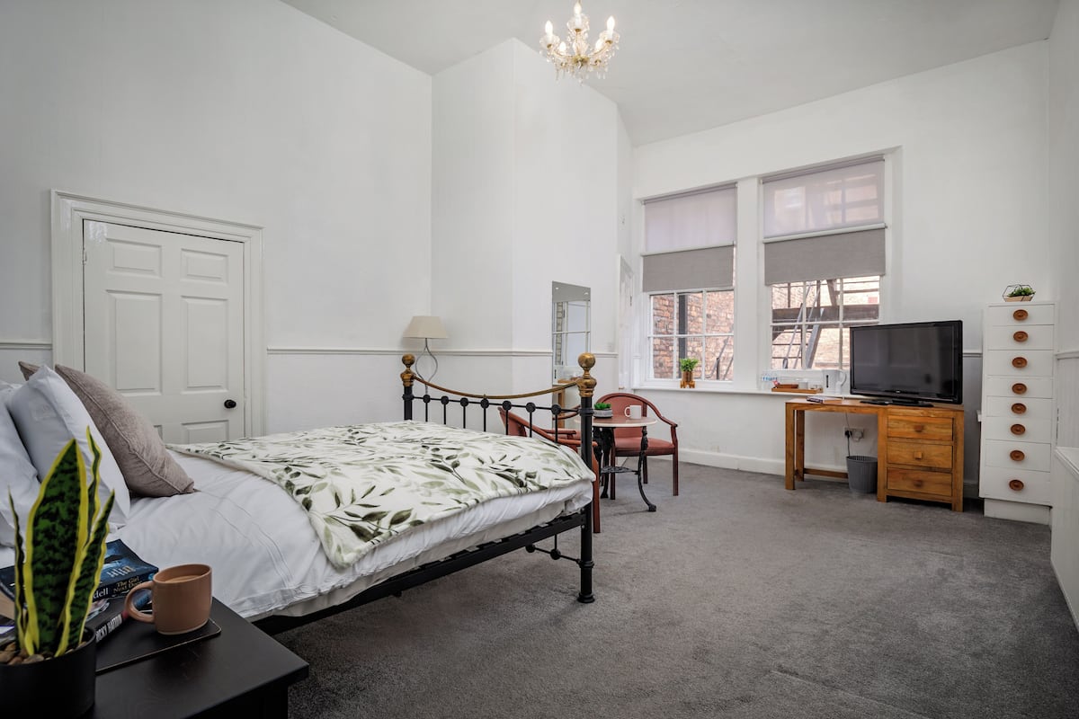 Une chambre à coucher comprenant un lit, un bureau, une chaise, un téléviseur et une fenêtre avec des stores.