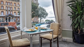 Et morgenbord med tallerkener, en kande og en kop, placeret ved et vindue med udsigt over en by med historiske bygninger og parkerede biler.