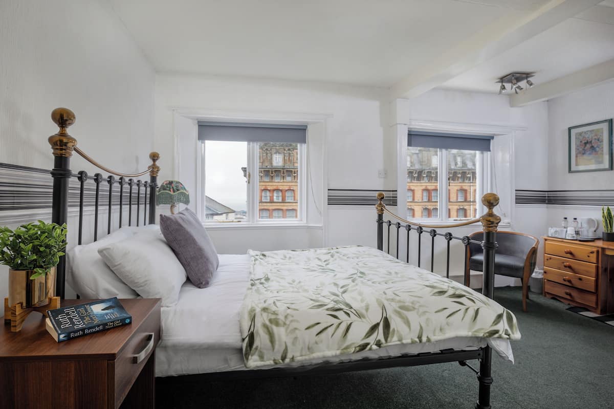 Une chambre bien rangée, avec un lit, une table de chevet et une vue sur les bâtiments par la fenêtre.