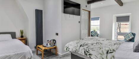 A bedroom with two beds, a TV, a radiator, a small table with a kettle, and a window with blinds.